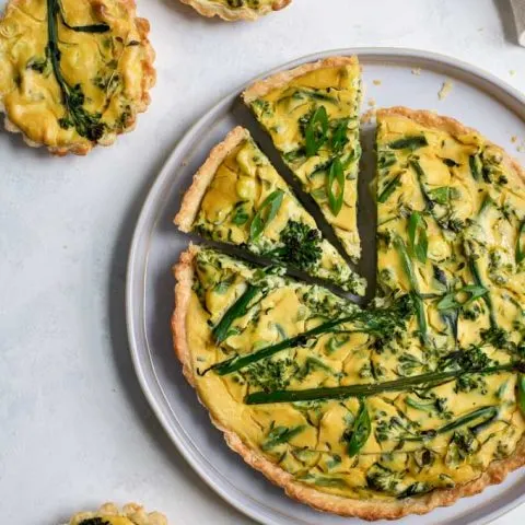 vegan sprouting broccoli quiche with two slices cut into it and three mini quiches aroud it