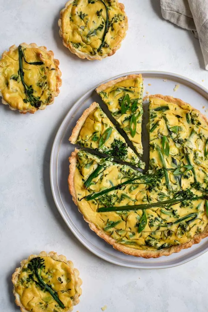 vegan sprouting broccoli quiche with two slices cut into it and three mini quiches aroud it