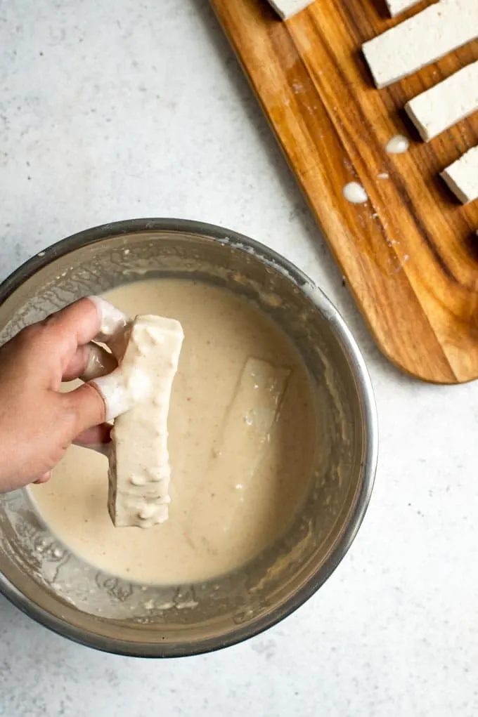 a hand is shown dipping the tofu into the batter for the tacos