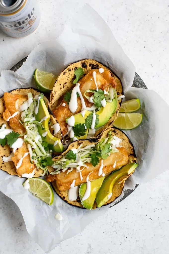 three Baja tofu tacos with avocado and lime wedges, served with a Modelo beer