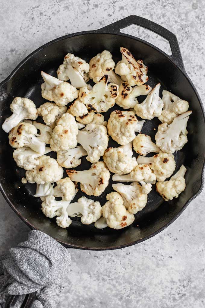 cauliflower after being sautÃ©ed in a cast iron skillet before cooking the curry, some char is visible on the florets.