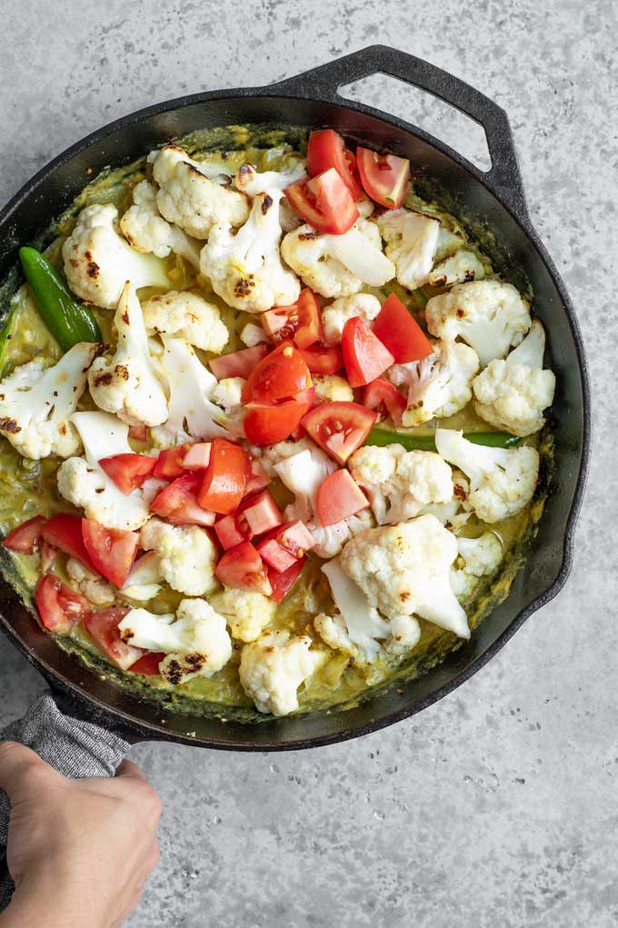 The curry once the vegetables have been added, in a cast iron skillet with a hand grabbing the handle, which is wrapped in a napkin