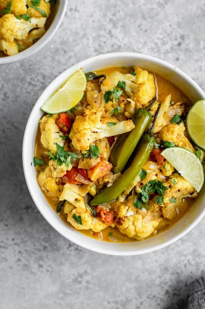 cauliflower moilee curry in a bowl garnished with cilantro and two cooked green chiles in the center of the bowl