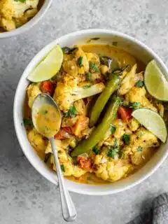 some of the moilee curry broth in a spoon resting on a bowl of the curry