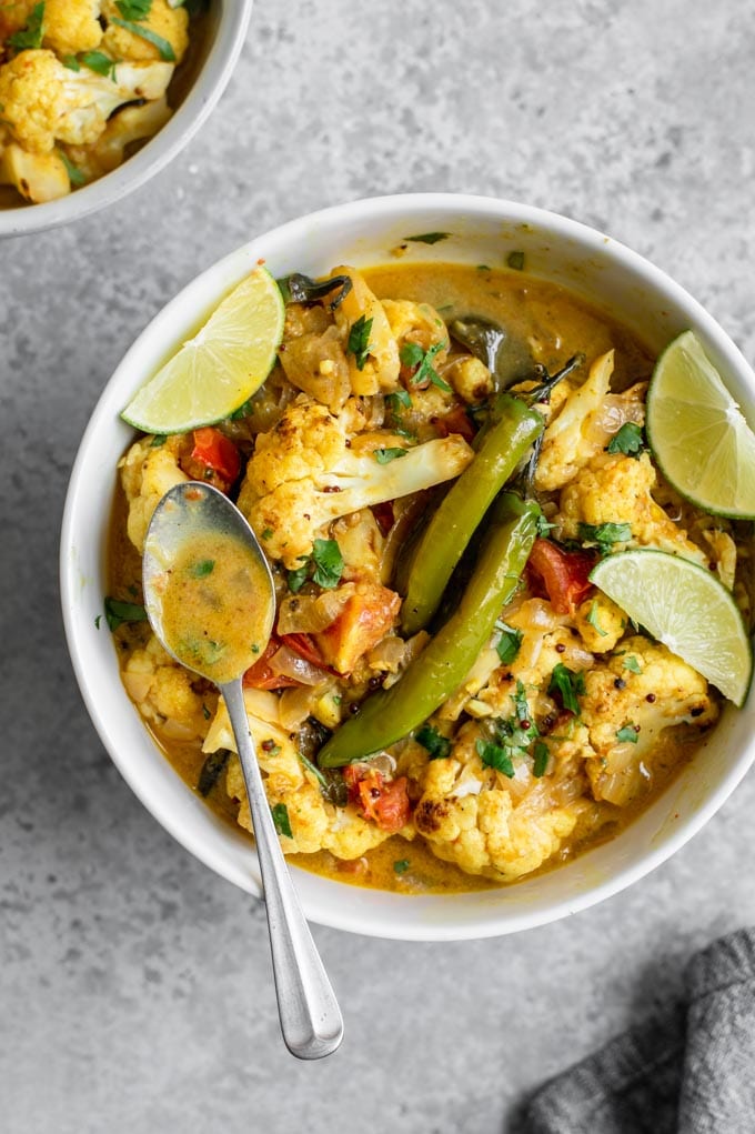 some of the moilee curry broth in a spoon resting on a bowl of the curry