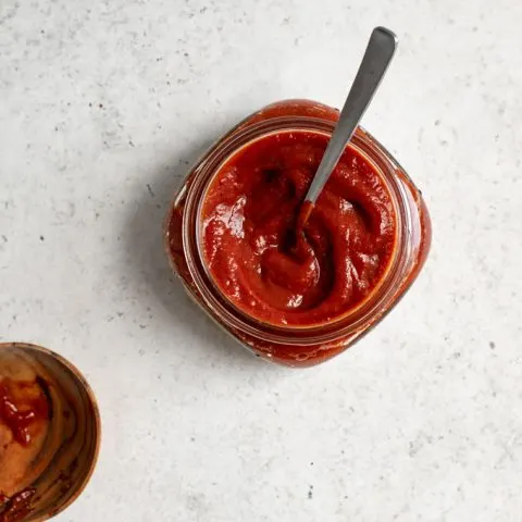 chipotle barbecue sauce in a small jar with a spoon in it and a used spoon rest