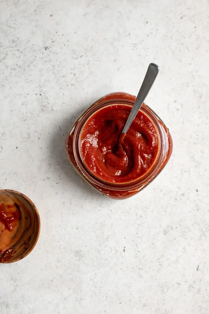chipotle barbecue sauce in a small jar with a spoon in it and a used spoon rest