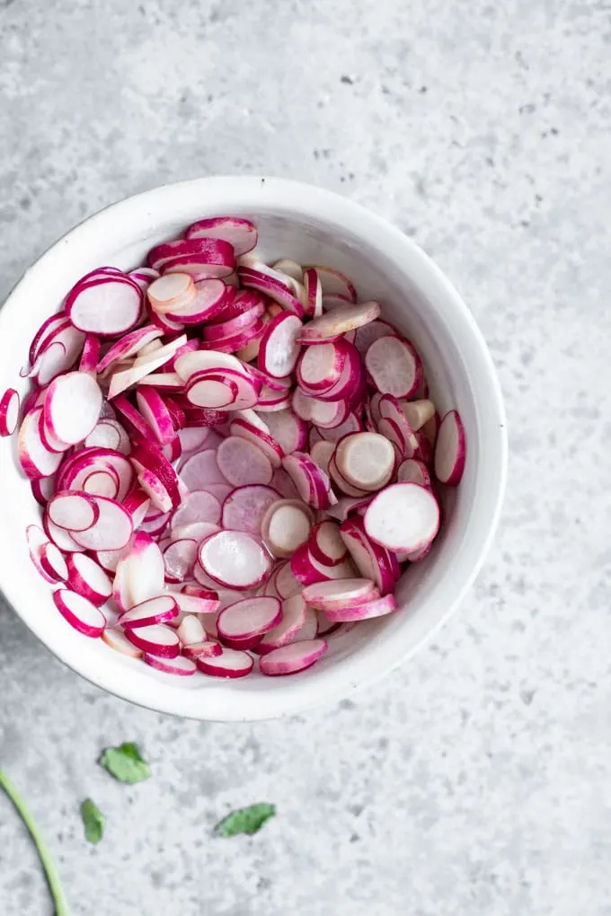the thinly sliced radishes in a bowl after being salted with water released from the radishes pooling at the bottom of the bowl