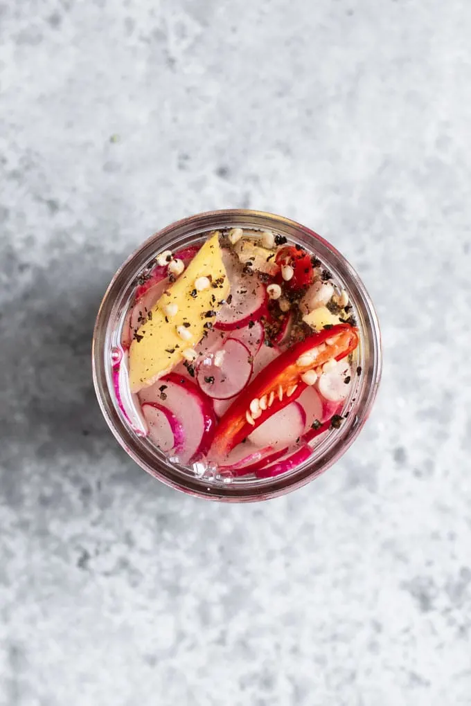 radishes, ginger, and a sliced chile in a jar with spices, covered with rice vinegar