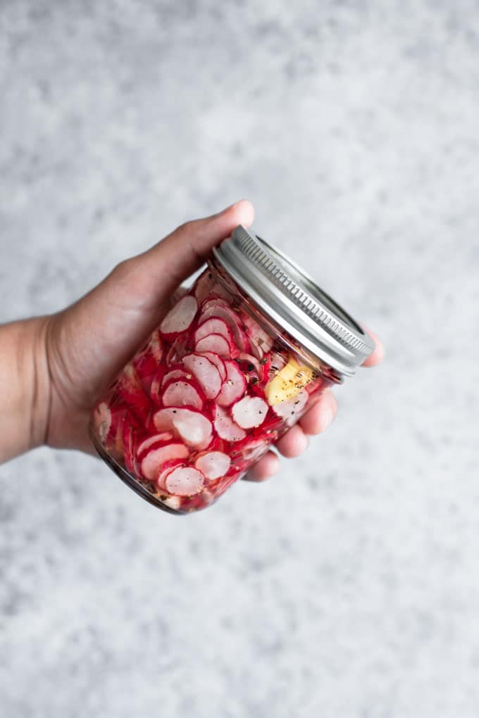 radishes just mixed with the spices and vinegar in a glass jar, being held up by a hand