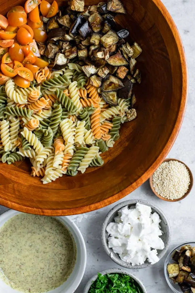 all the ingredients for the pasta salad: pasta, roasted eggplant, cherry tomatoes, za'atar vinaigrette, vegan feta, parsley, and toasted sesame seeds