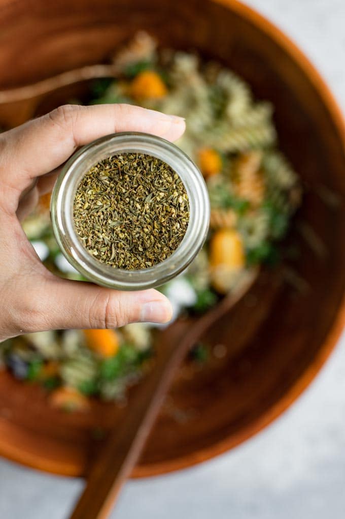 close up of the za'atar spice blend held overtop the pasta salad, which is blurred out in the background