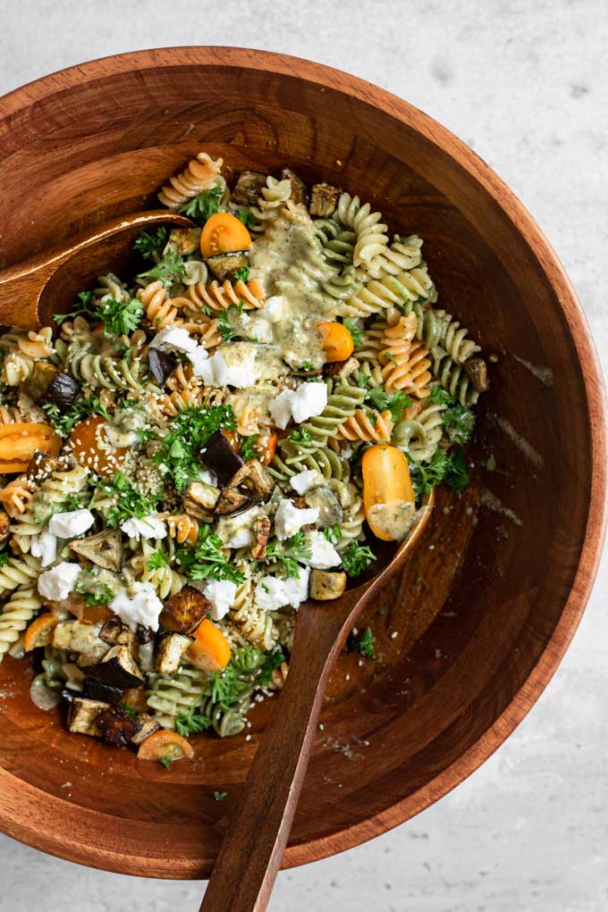 tossing together the ingredients for the pasta salad with two large wooden spoons in a wooden salad bowl