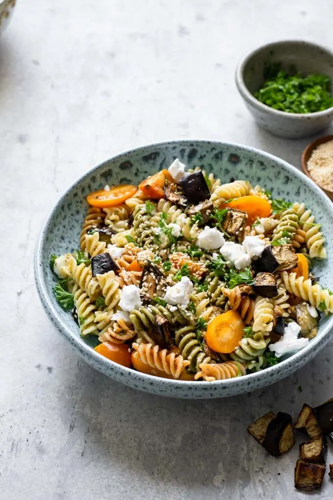 pasta salad served in a blue ceramic bowl with bowls of parsley and toasted sesame seeds on the side for garnish