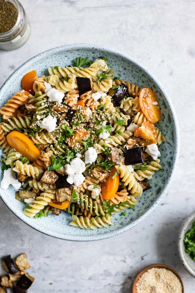 overhead view of the za'atar pasta salad served in a bowl with sides of the garnishes and eggplant on the edges of the photo