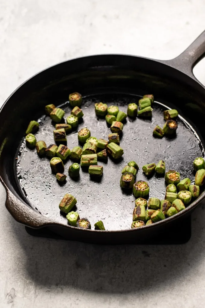 Okra cooked in the skillet right before the spices have been added, the okra has shrunk and turned golden in spots