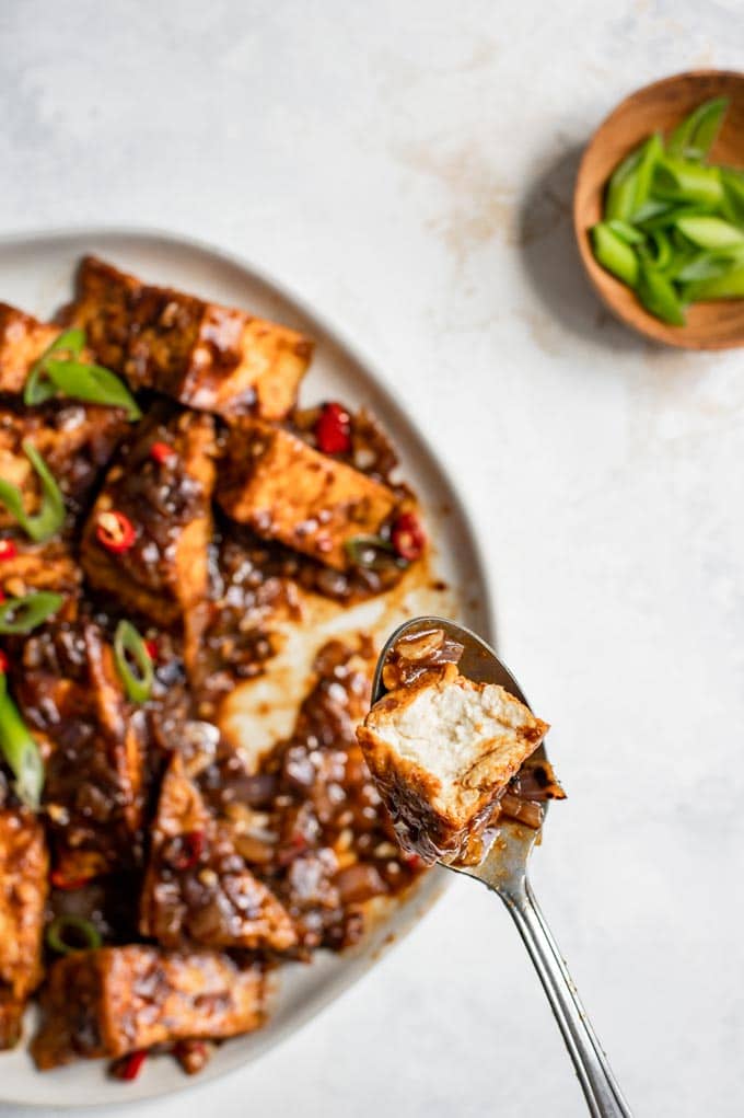 a spoon with a cut piece of tofu from the black bean sauce tofu dish