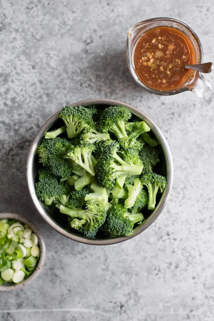 the mise en place of the ingredients: broccoli cut into florets, sliced scallions, and the prepared sauce