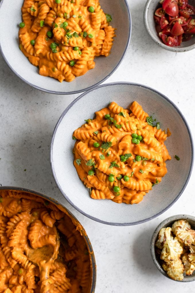 the pot of curry mac and cheese and two prepared bowls, with a side of roasted cauliflower and a side of diced cherry tomatoes