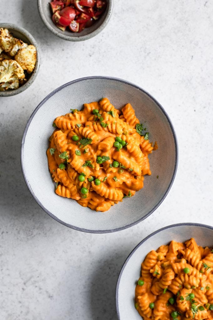 two bowls of pasta with a side of curry roasted cauliflower and a side of tomatoes