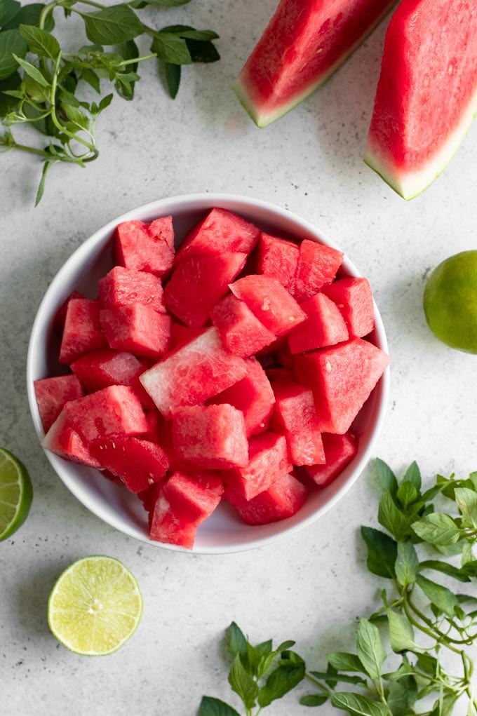 ingredients for agua frescas: bowl of cut watermelon, mint, cut lime, with a couple wedges of watermelon in the corner of the photo