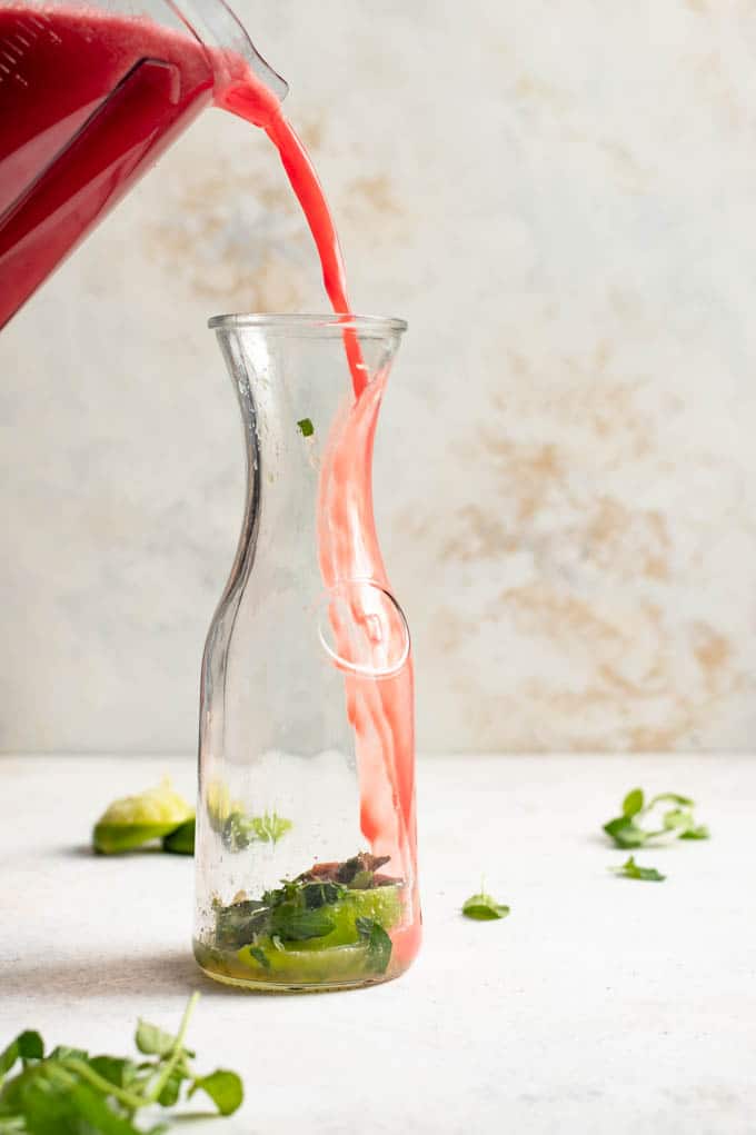 pouring the blended watermelon juice into a pitcher with the muddled mint and lime at the bottom