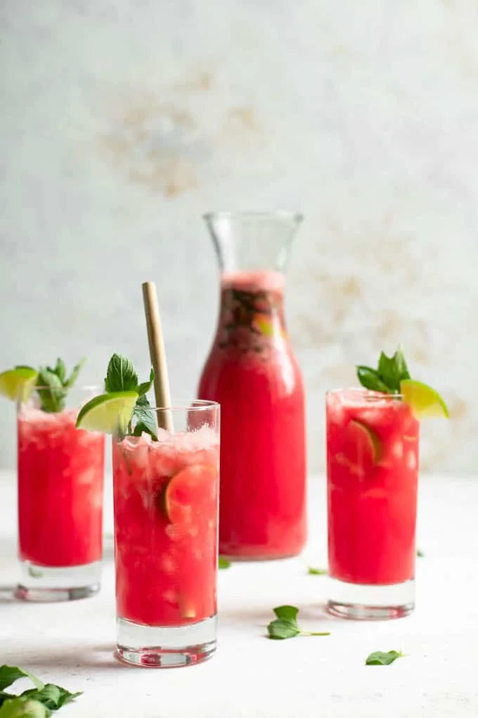 three glasses of watermelon mint agua fresca with the pitcher in the background