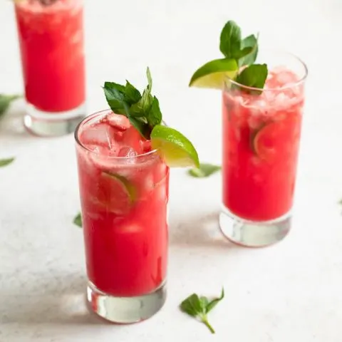 watermelon mint agua frescas in three glasses garnished with lime wedges and mint