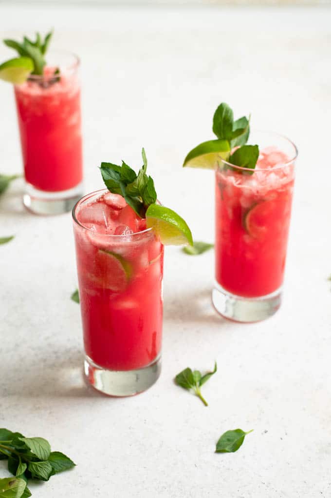 watermelon mint agua frescas in three glasses garnished with lime wedges and mint