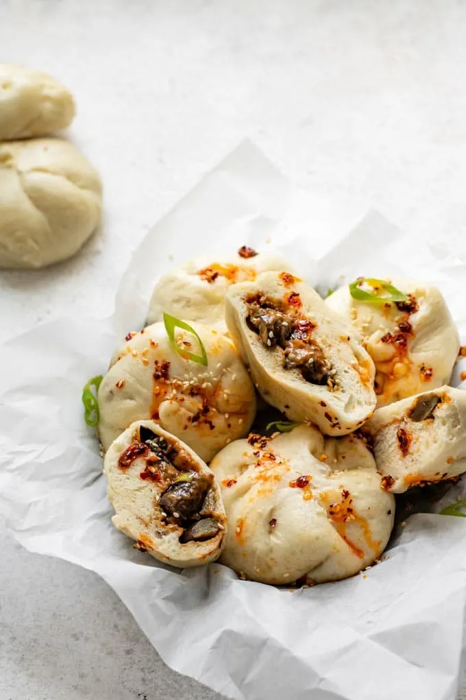 hoisin eggplant bao in a basket drizzled with chili oil with one cut open to show the filling