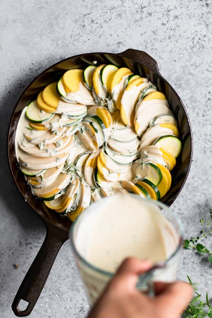 the herb filled cream sauce being poured over the prepared potato and zucchini