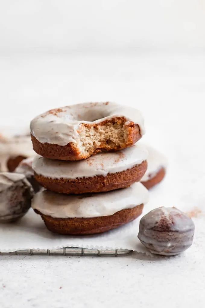 vegan maple glazed apple cider donuts stacked with a bite out of the top one