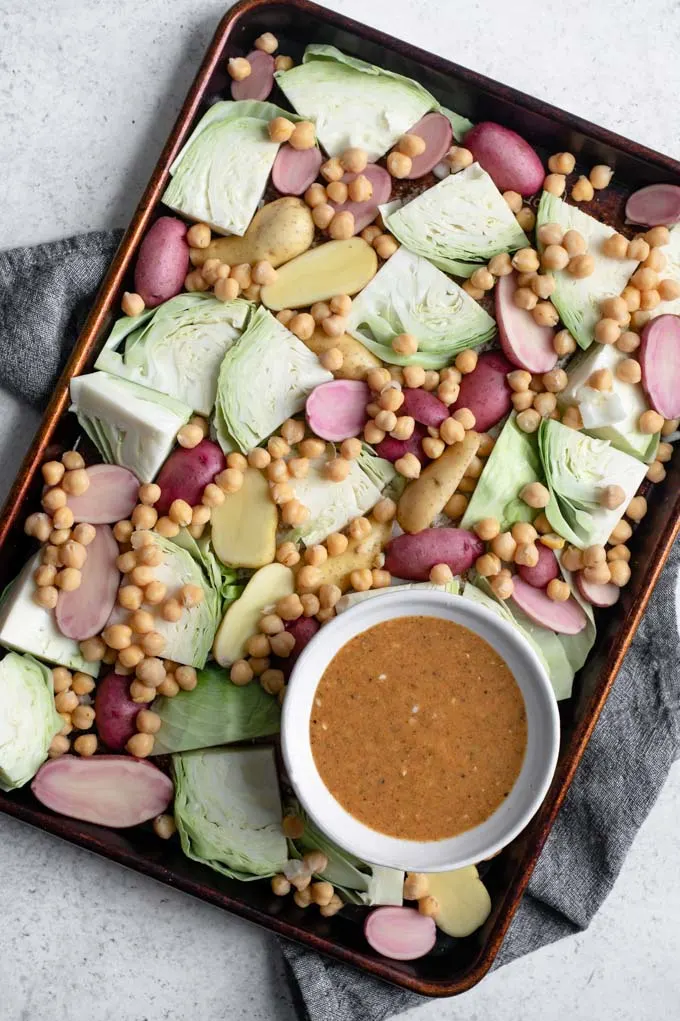 cabbage, potatoes, and chickpeas on a sheet pan with a bowl of mustard vinaigrette on the side