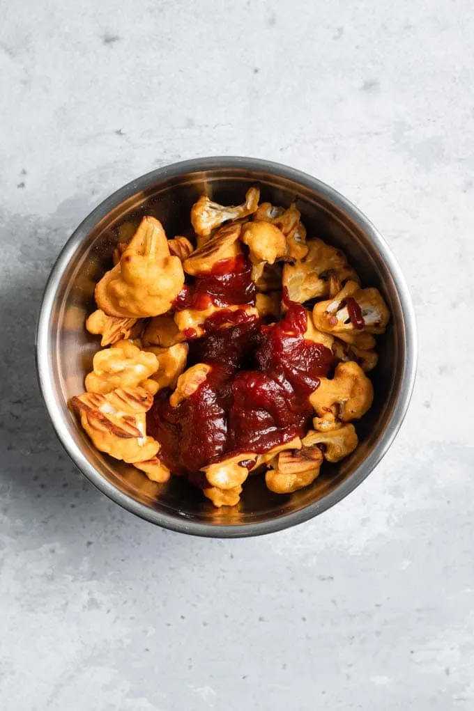 cauliflower wings in a mixing bowl with barbecue sauce poured over them
