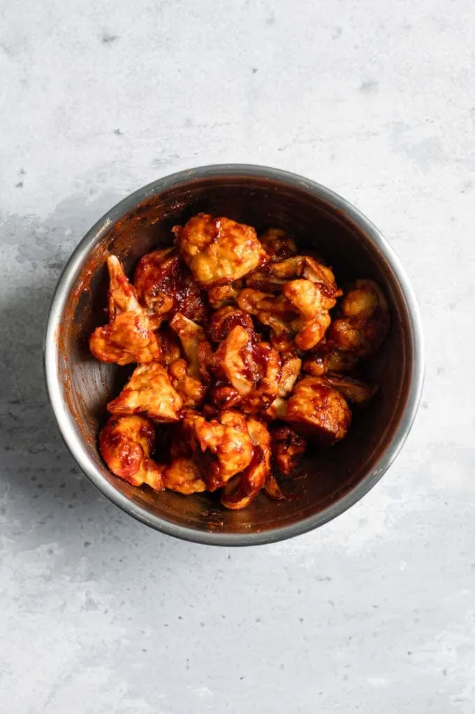 cauliflower wings tossed in cranberry barbecue sauce in a mixing bowl