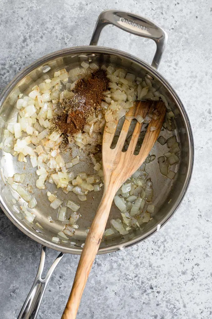 adding spices to onion, garlic, and cumin in pan