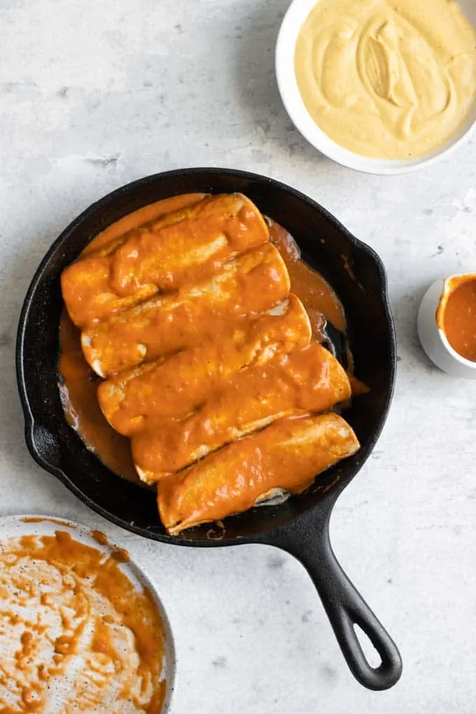 tortillas stuffed with lentil filling and smothered in enchilada sauce in a skillet