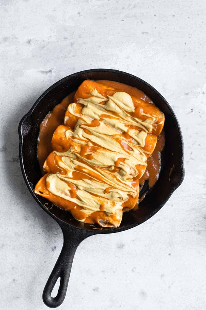 enchiladas smothered with enchilada sauce and butternut queso ready to bake