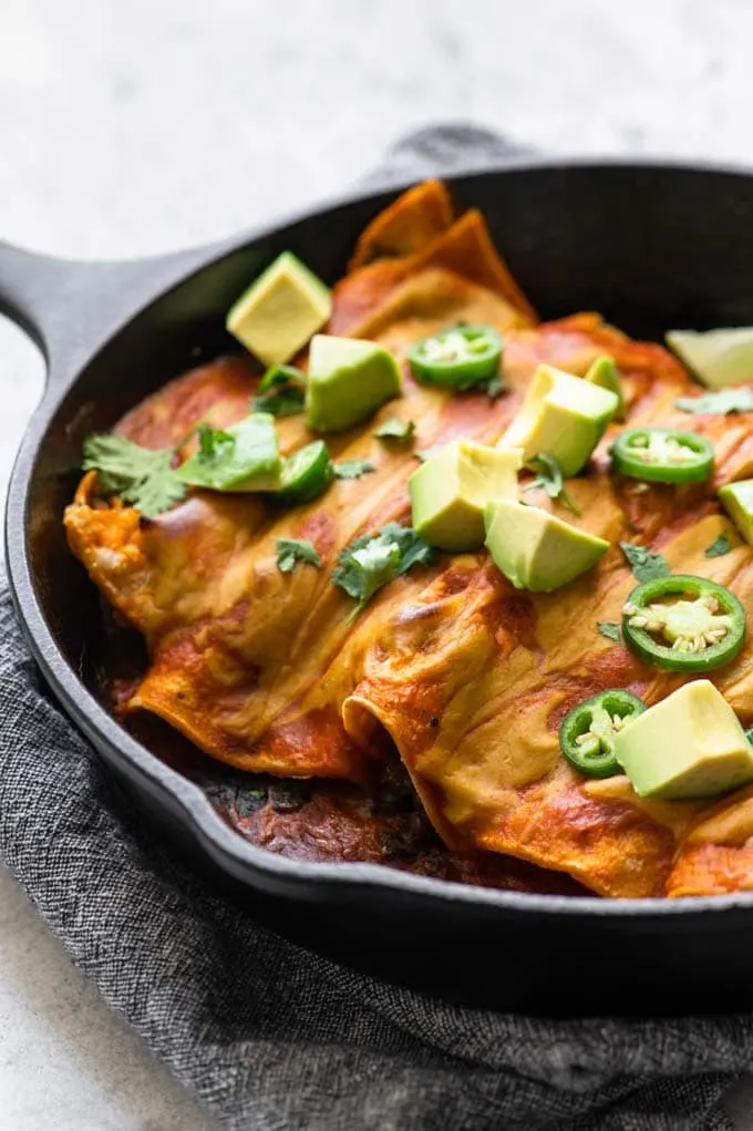 enchiladas baked in a skillet and topped with avocado and jalapeño