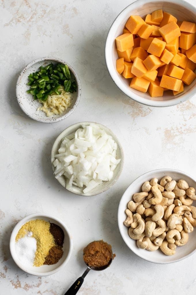 ingredients prepped and set out for butternut queso: butternut squash, cashews, onion, garlic, jalapeño, seasoning, and miso paste