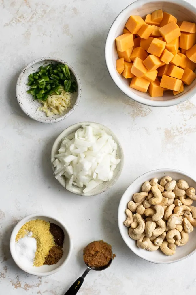 ingredients prepped and set out for butternut queso: butternut squash, cashews, onion, garlic, jalapeño, seasoning, and miso paste