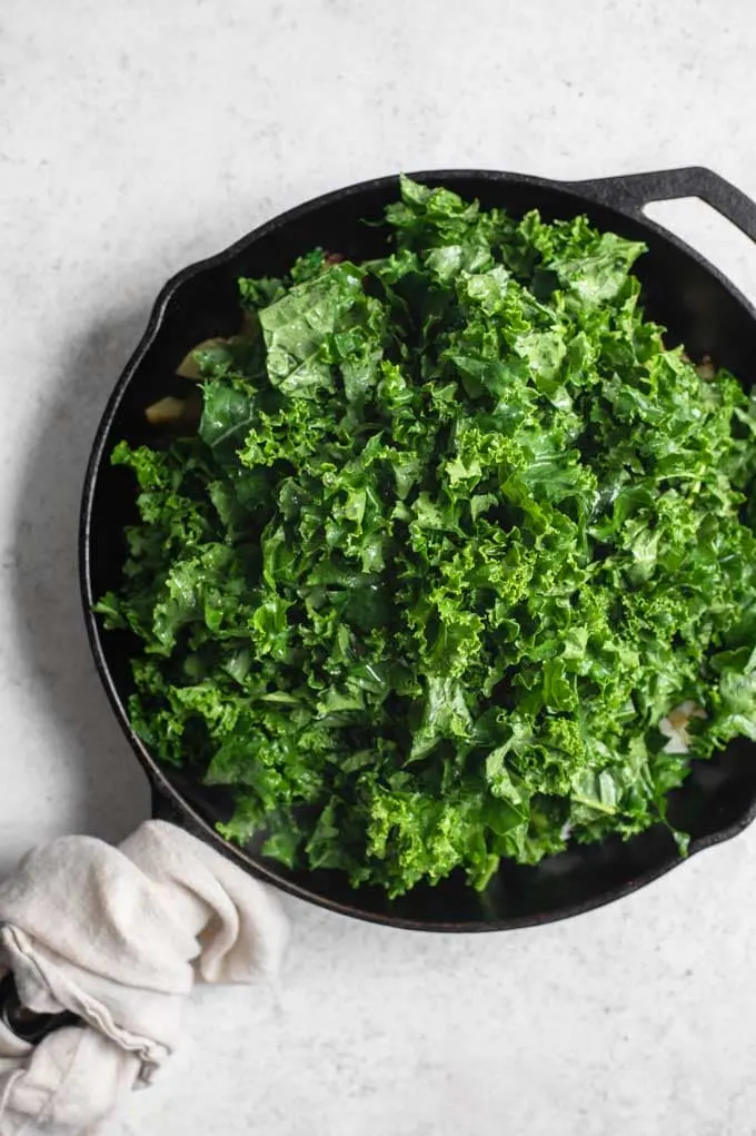 kale added to cooked potatoes, onion, and garlic in pan