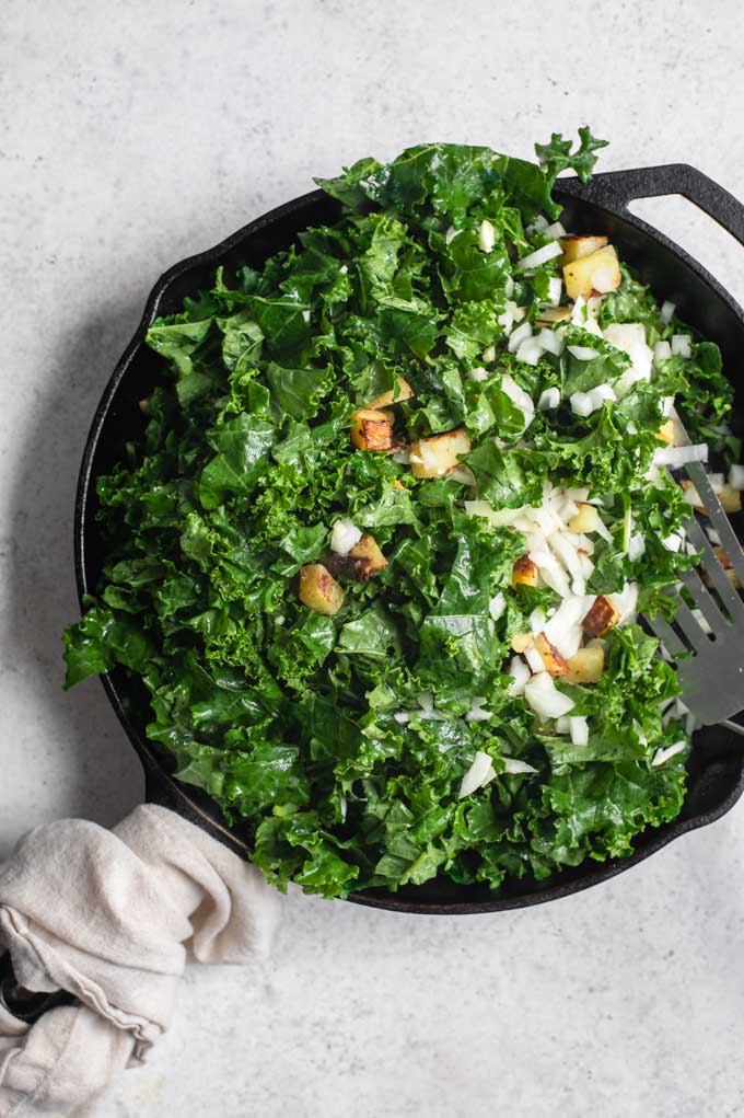 kale, onion, and garlic added to cooked potatoes in skillet