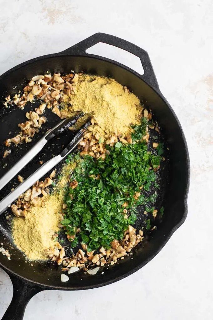 adding nutritional yeast and parley to the toasted walnuts and garlic