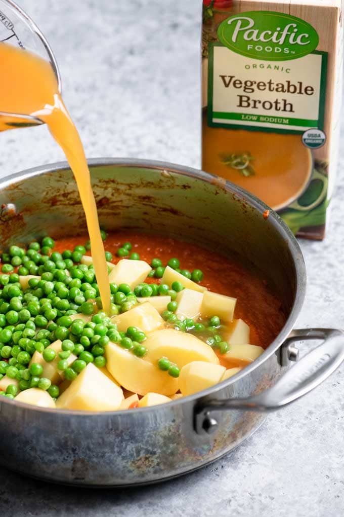 pouring Pacific Foods Low Sodium Vegetable Broth into the pot with curry tomato sauce, potatoes, and peas