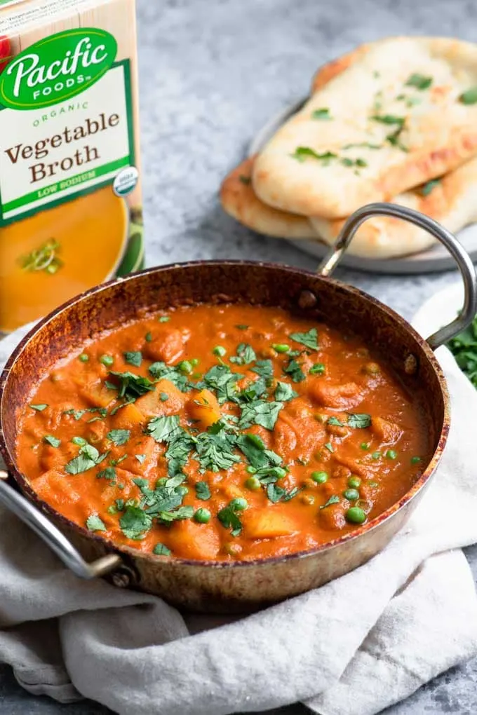 aloo matar in a serving dish with pacific foods low sodium vegetable broth in background