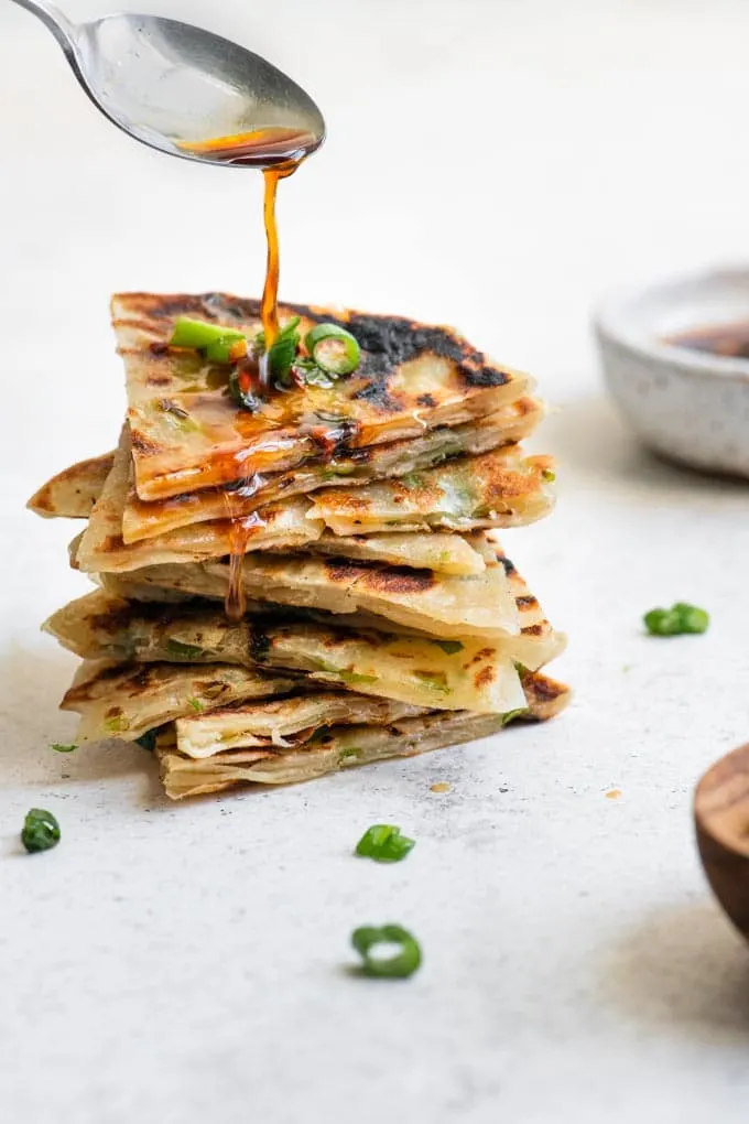 drizzling dipping sauce over a stack of scallion pancake wedges