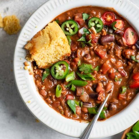 vegan chili with toppings mixed into the stew and a piece of cornbread tucked into the bowl