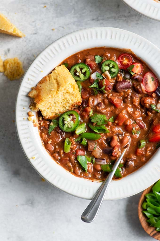 vegan chili with toppings mixed into the stew and a piece of cornbread tucked into the bowl