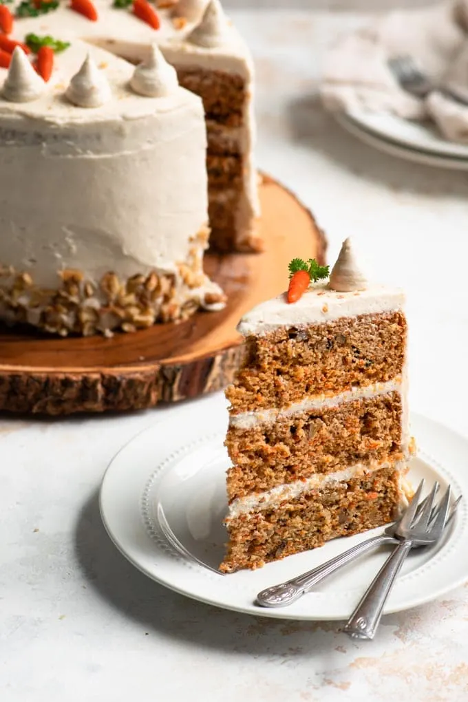 slice of carrot cake upright on a plate and full cake in the background